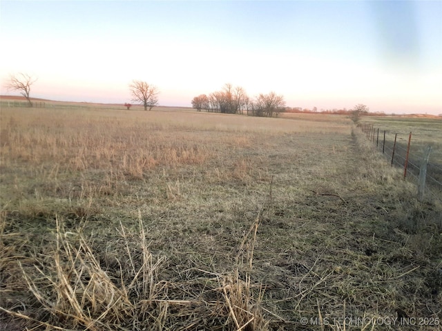 yard at dusk featuring a rural view and fence