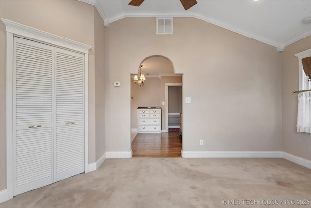 carpeted empty room featuring a ceiling fan, baseboards, crown molding, arched walkways, and a chandelier