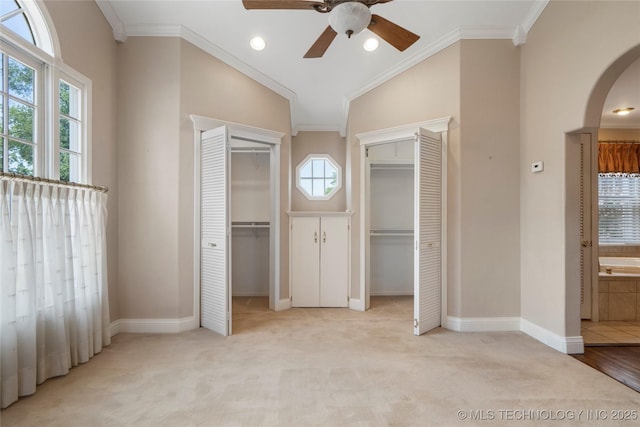 unfurnished bedroom featuring two closets, arched walkways, light carpet, crown molding, and vaulted ceiling