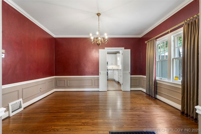unfurnished dining area featuring a chandelier, wood finished floors, crown molding, a decorative wall, and a wainscoted wall