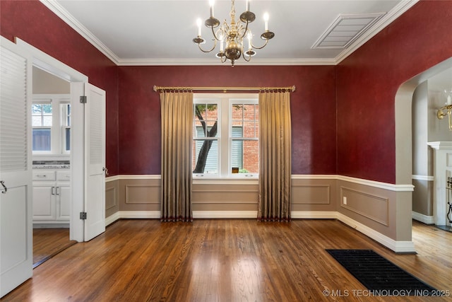 unfurnished dining area featuring a chandelier, arched walkways, wood finished floors, a wainscoted wall, and ornamental molding