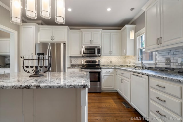 kitchen with stainless steel appliances, a sink, ornamental molding, white cabinets, and decorative backsplash