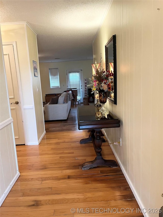 corridor with light wood finished floors, a textured ceiling, and ornamental molding