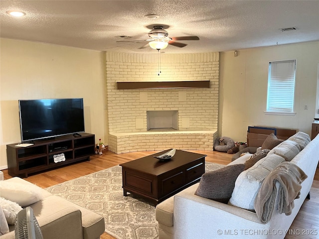 living room featuring a ceiling fan, a textured ceiling, wood finished floors, and a fireplace