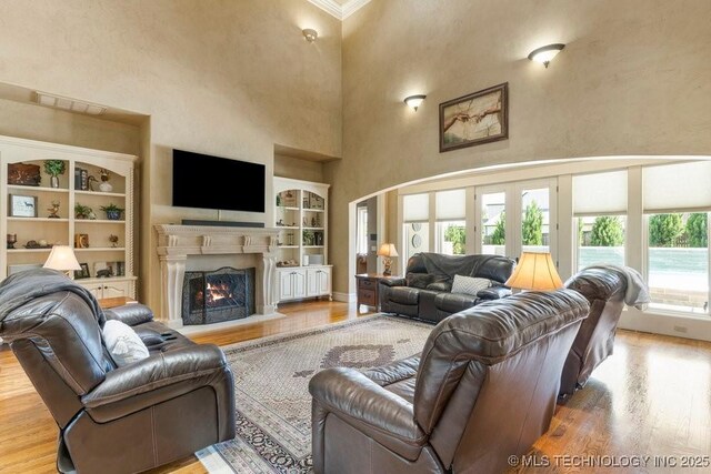 716 W 108th Pl S, Jenks, OK 74037 - living room with built in shelves, wood finished floors, a towering ceiling, a lit fireplace, and crown molding