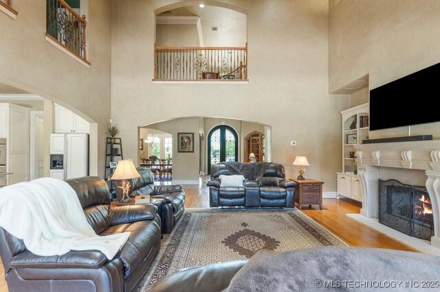 716 W 108th Pl S, Jenks, OK 74037 - living area with arched walkways, a high ceiling, light wood-style flooring, a warm lit fireplace, and baseboards