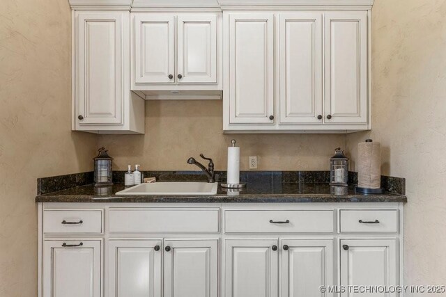 716 W 108th Pl S, Jenks, OK 74037 - kitchen featuring a sink, white cabinetry, a textured wall, and dark stone countertops
