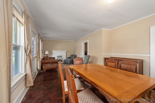 dining area with dark wood-style flooring, crown molding, a stone fireplace, and baseboards