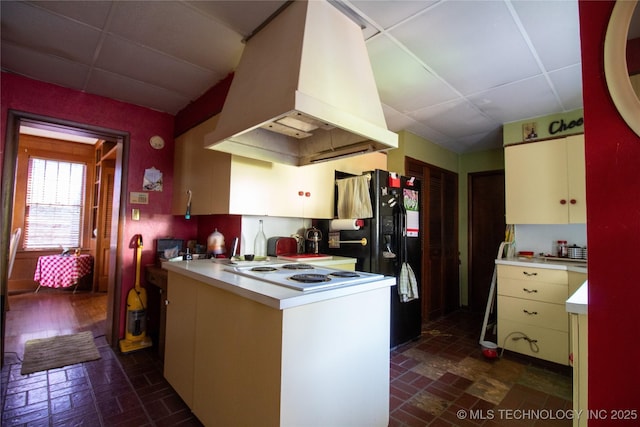 kitchen with custom exhaust hood, brick patterned floors, a drop ceiling, light countertops, and black fridge