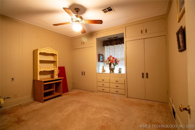 unfurnished bedroom featuring light colored carpet, ornamental molding, multiple closets, and a ceiling fan