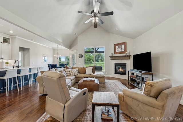 living room featuring dark wood-type flooring, a glass covered fireplace, a ceiling fan, high vaulted ceiling, and a chandelier