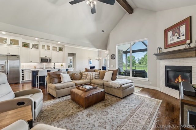 living area with beam ceiling, dark wood finished floors, a ceiling fan, high vaulted ceiling, and a brick fireplace