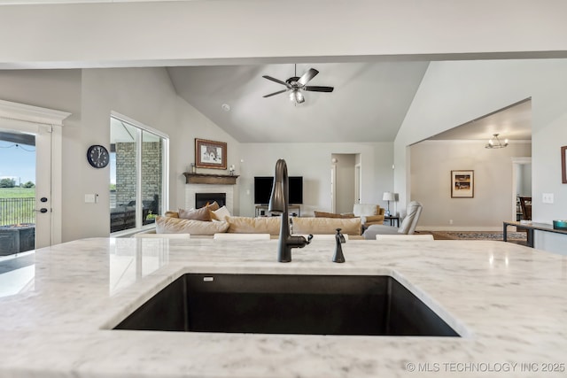 kitchen featuring a sink, light stone countertops, ceiling fan, a fireplace, and open floor plan