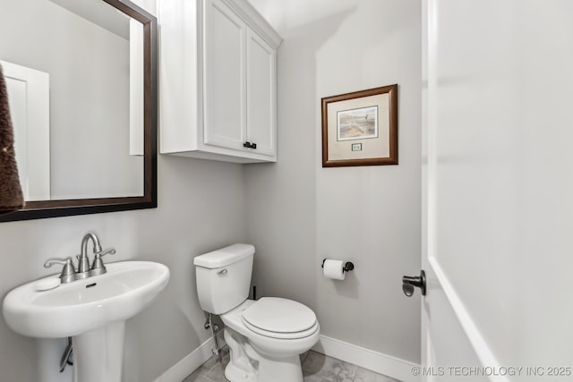 half bath featuring baseboards, toilet, marble look tile flooring, and a sink