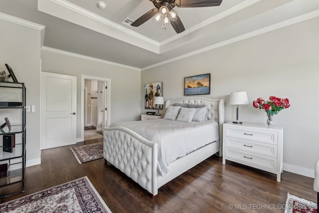 bedroom with a raised ceiling, dark wood-style floors, crown molding, baseboards, and ensuite bath