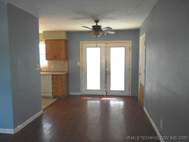 unfurnished dining area with ceiling fan, wood finished floors, baseboards, and french doors