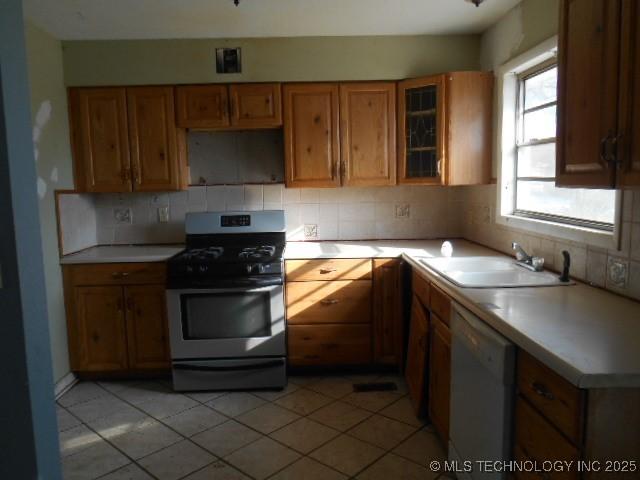 kitchen with stainless steel range with gas cooktop, dishwasher, a sink, tasteful backsplash, and light countertops