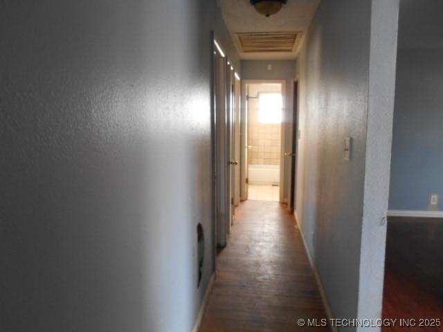 hallway with wood finished floors, baseboards, and a textured wall