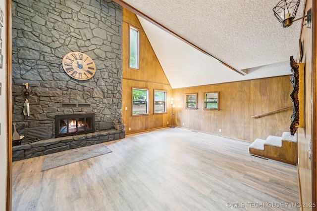 205 Woods Dr, Bernice, OK 74331 - unfurnished living room featuring high vaulted ceiling, a textured ceiling, wooden walls, wood finished floors, and a fireplace