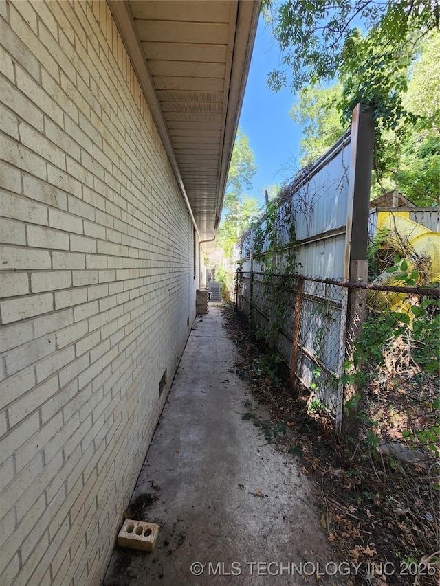view of home's exterior with fence, brick siding, and central AC unit