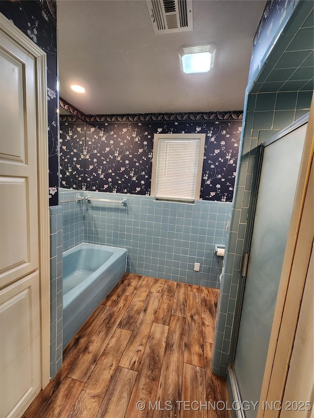 full bath featuring wallpapered walls, tile walls, wood finished floors, a bath, and a stall shower