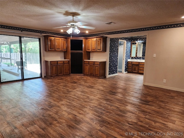 unfurnished living room featuring dark wood-type flooring, a textured ceiling, baseboards, and ceiling fan