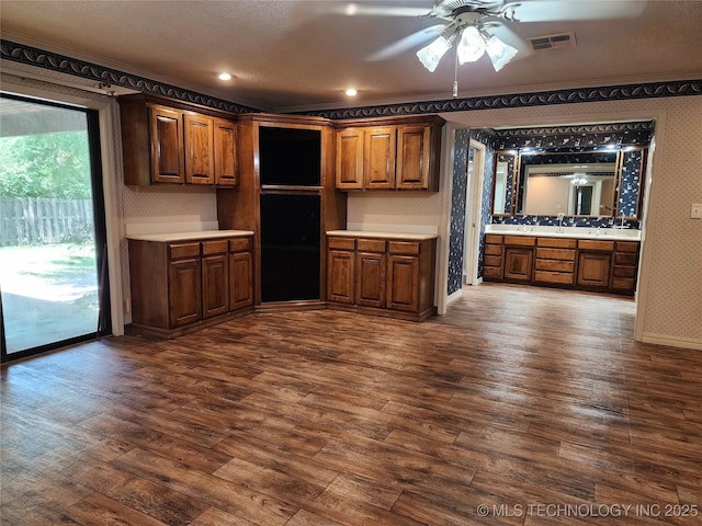 kitchen with wallpapered walls, light countertops, dark wood-type flooring, ornamental molding, and ceiling fan