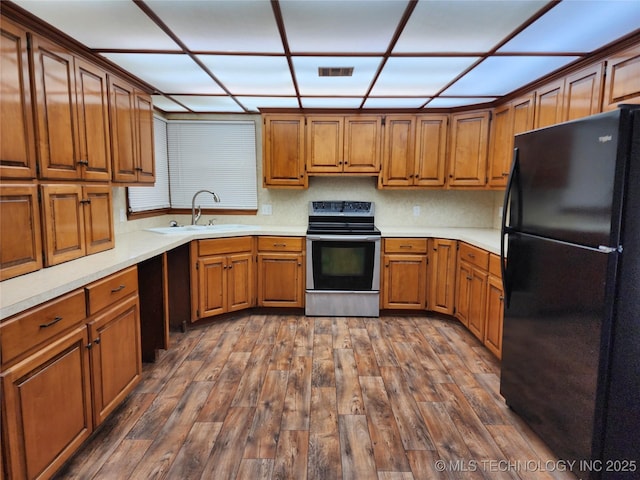 kitchen featuring freestanding refrigerator, electric stove, a sink, and brown cabinets