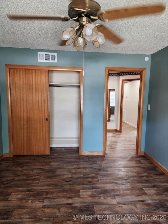 unfurnished bedroom featuring dark wood finished floors, a closet, baseboards, a ceiling fan, and a textured ceiling