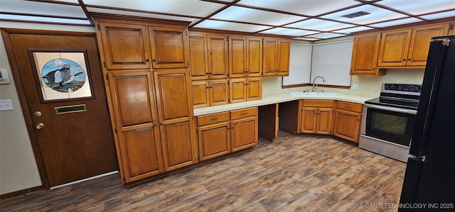 kitchen featuring a sink, electric stove, brown cabinetry, light countertops, and dark wood-style floors