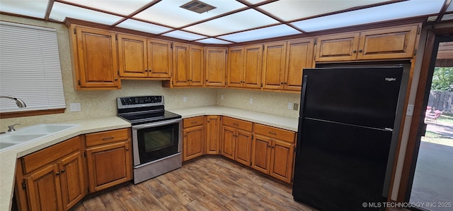 kitchen featuring freestanding refrigerator, stainless steel electric range, a sink, and brown cabinetry