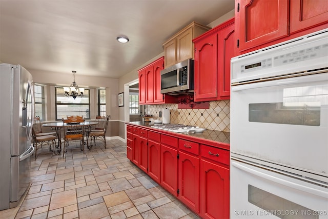 kitchen featuring appliances with stainless steel finishes, a chandelier, light stone finish floors, decorative backsplash, and baseboards
