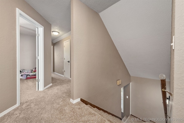 corridor with a textured ceiling, carpet flooring, and baseboards