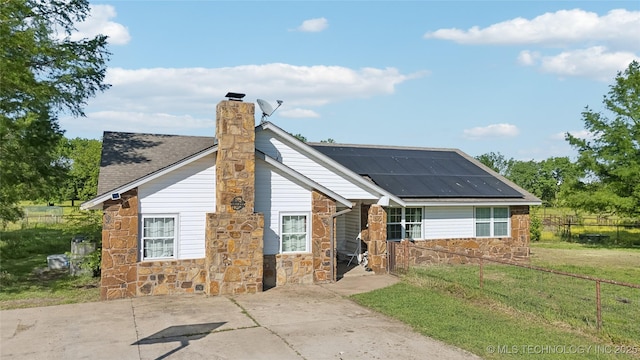 view of front of house featuring stone siding, roof mounted solar panels, and a chimney