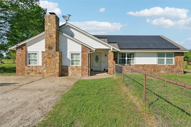 ranch-style house with stone siding, solar panels, and a chimney
