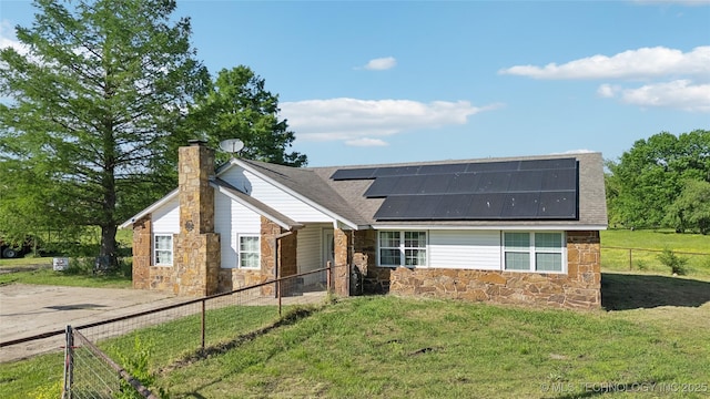 view of front of property with stone siding, solar panels, a chimney, and a shingled roof