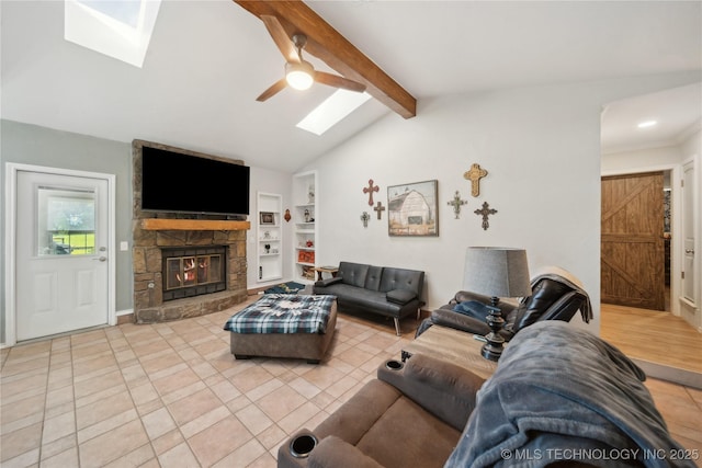 living area featuring a skylight, built in shelves, a stone fireplace, ceiling fan, and tile patterned floors