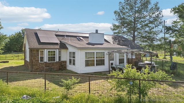 back of property featuring solar panels, stone siding, roof with shingles, a chimney, and a fenced backyard
