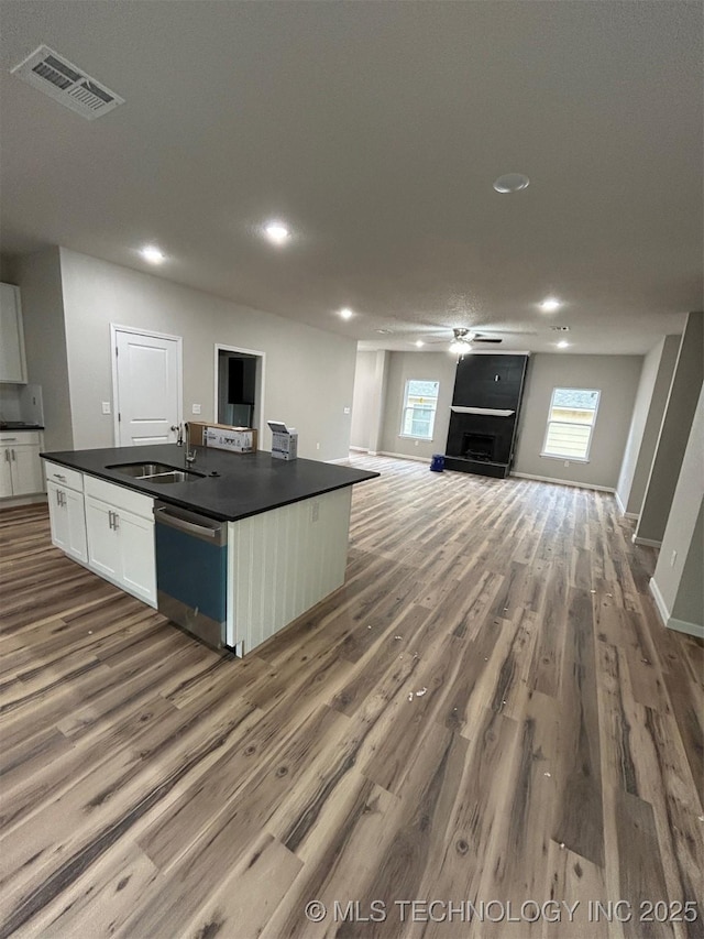 kitchen with stainless steel dishwasher, a sink, dark countertops, white cabinets, and dark wood-type flooring