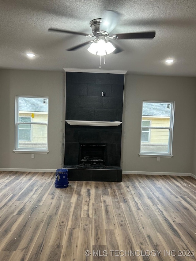 unfurnished living room with a textured ceiling, wood finished floors, ceiling fan, and baseboards
