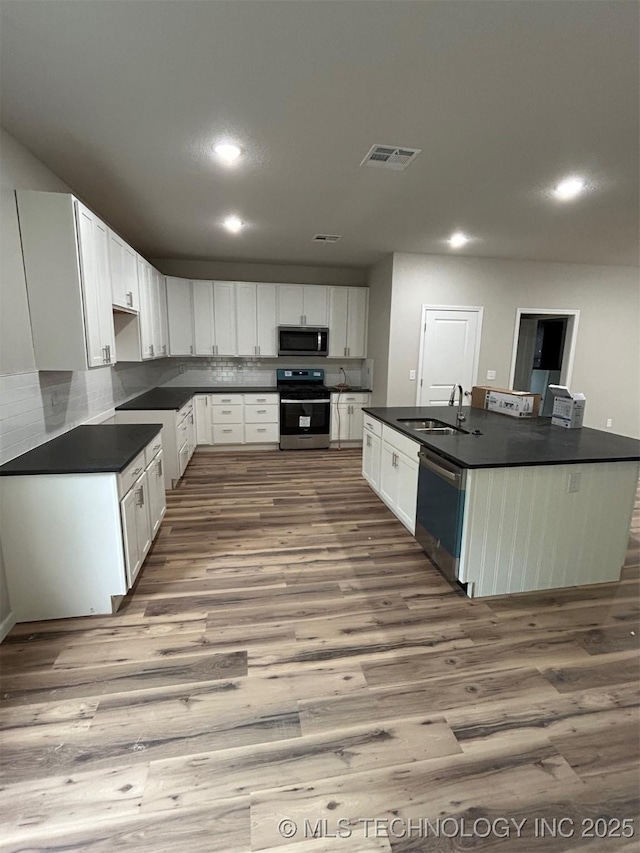 kitchen with stainless steel appliances, dark countertops, wood finished floors, a sink, and recessed lighting