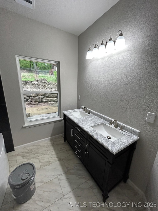 full bathroom featuring marble finish flooring, a textured wall, and double vanity
