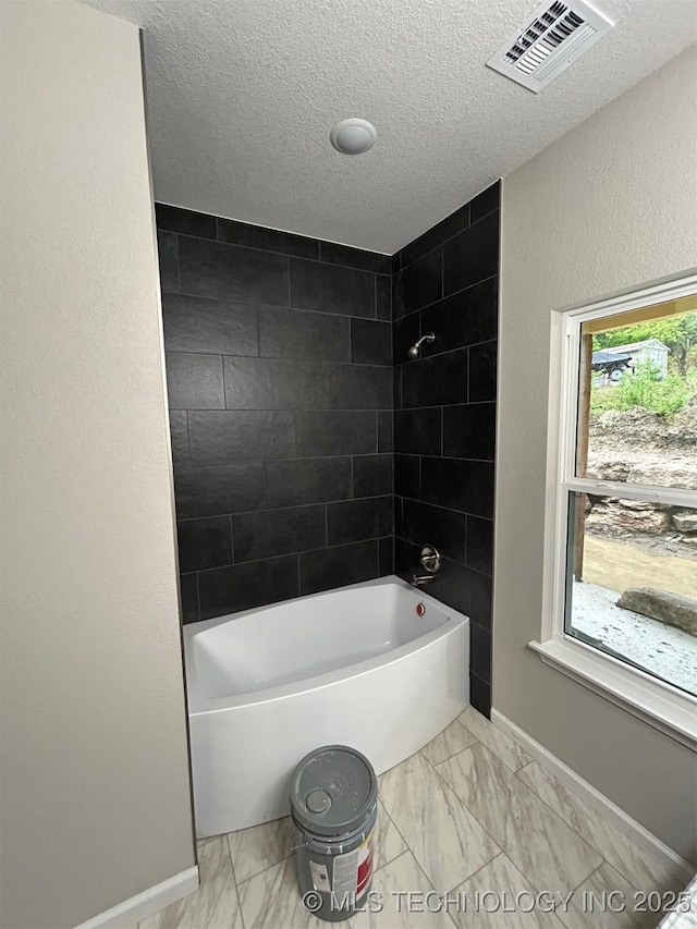 full bath with marble finish floors, shower / bathtub combination, baseboards, and a textured ceiling