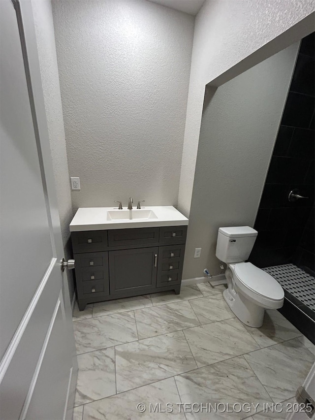full bathroom featuring vanity, toilet, marble look tiles, a textured wall, and baseboards
