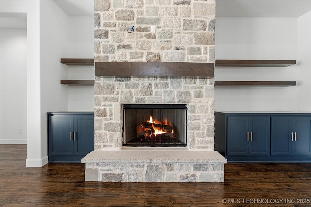 detailed view of wood finished floors, a stone fireplace, and baseboards