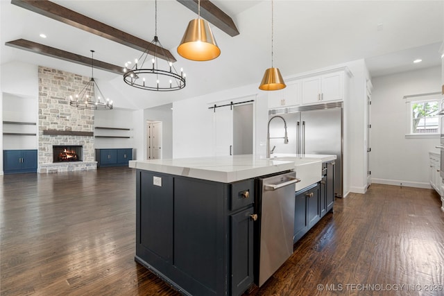 kitchen with stainless steel appliances, a barn door, a sink, white cabinetry, and pendant lighting