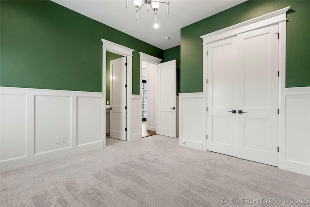 unfurnished bedroom with a decorative wall, carpet flooring, wainscoting, a closet, and a chandelier