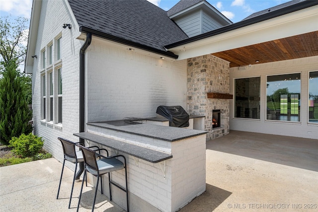 view of patio / terrace featuring an outdoor stone fireplace and a grill