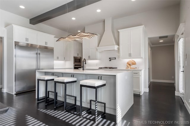 10616 N 81st E Pl, Owasso, OK 74055 - kitchen with custom exhaust hood, built in appliances, light countertops, white cabinetry, and a kitchen island with sink