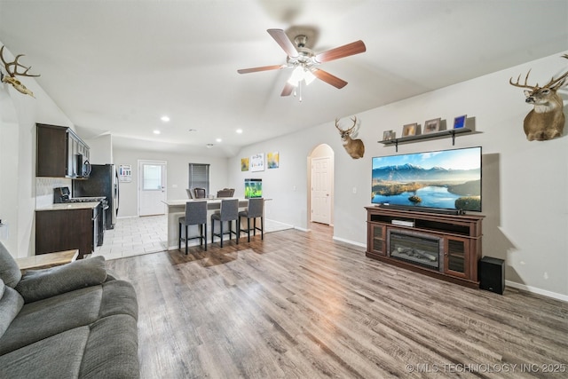 living room featuring arched walkways, light wood-style floors, a ceiling fan, recessed lighting, and baseboards
